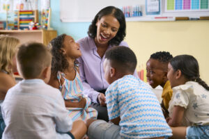 Speech-language pathologist smiling and engaging with a small group of elementary students during a classroom language lesson focused on communication and listening skills.