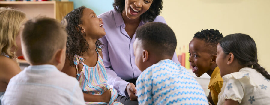 Speech-language pathologist smiling and engaging with a small group of elementary students during a classroom language lesson focused on communication and listening skills.