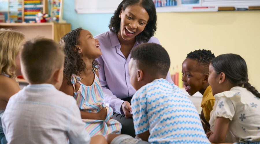 Speech-language pathologist smiling and engaging with a small group of elementary students during a classroom language lesson focused on communication and listening skills.